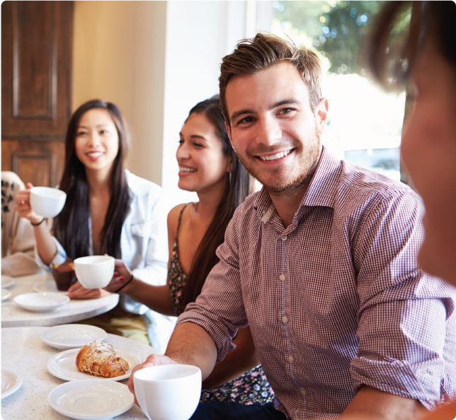 A close up on a young adult man drinking coffee with some friends