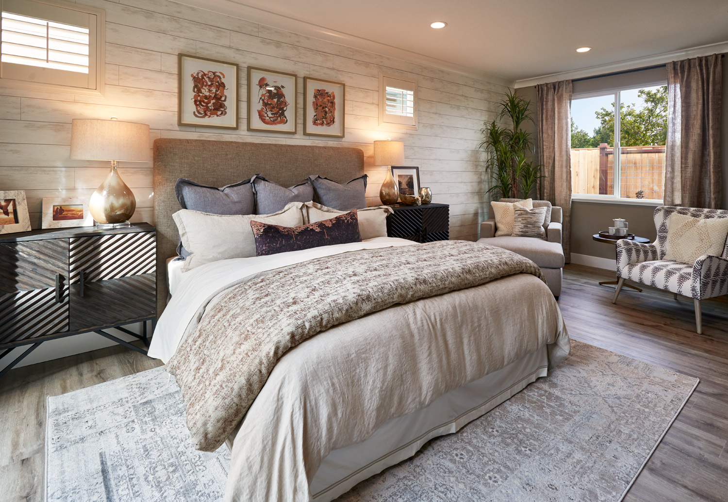 A large master bedroom with beige bedding and a shiplap accent wall